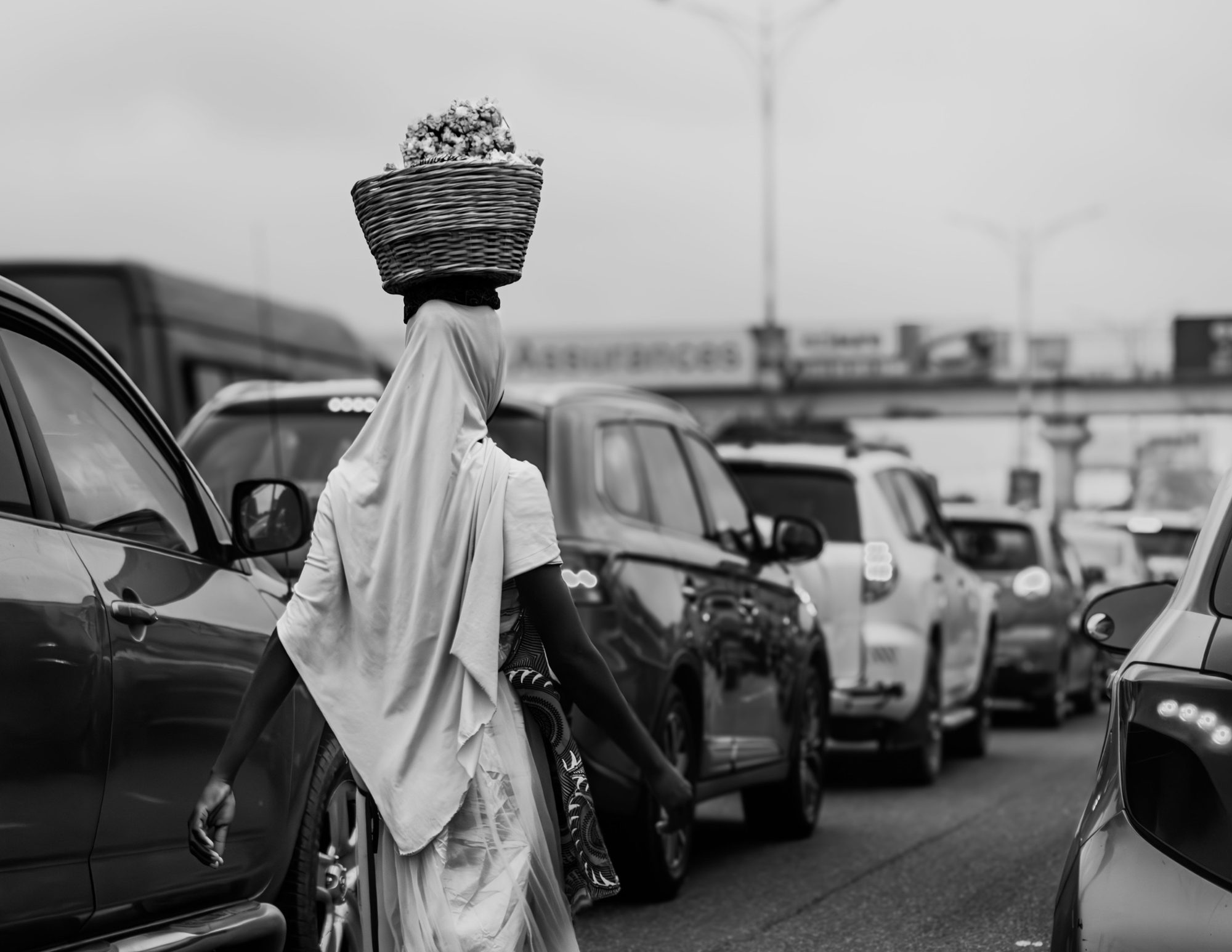A street trader carrying a basket, walking between cars in Accra traffic.